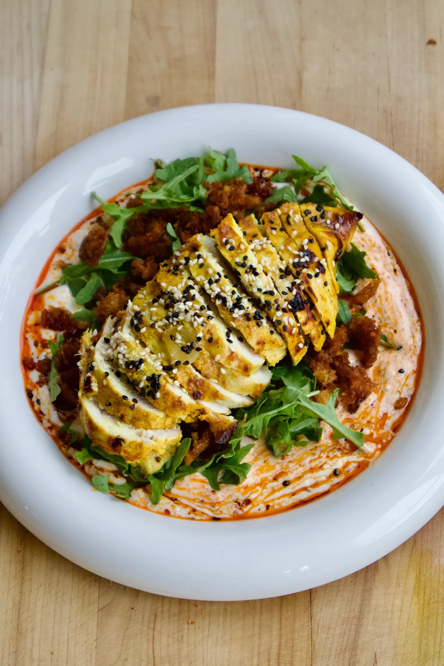 Crispy rice and chicken bowl with chili yoghurt, rocket, and sesame seeds