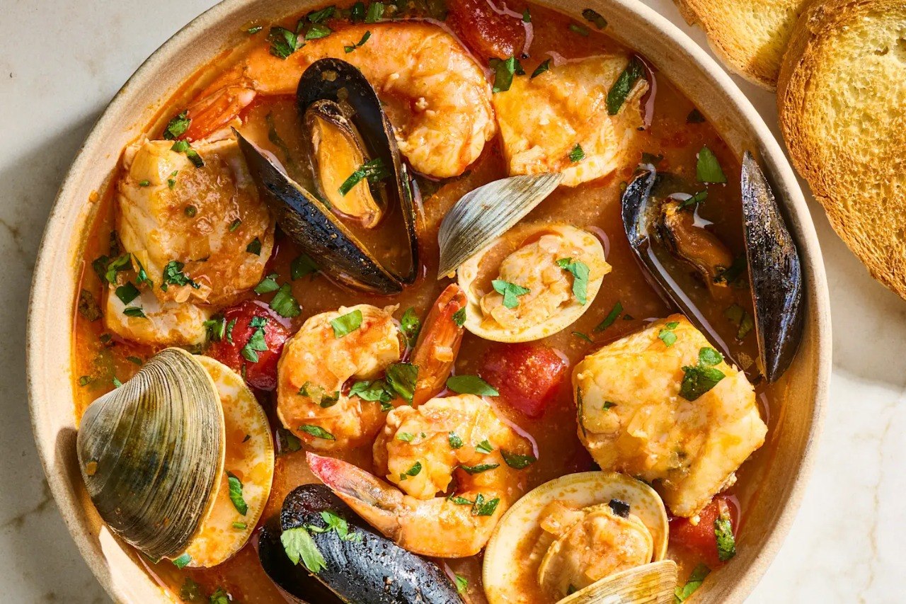 Bowl of cioppino with shrimp, mussels, clams, white fish, and toasted bread