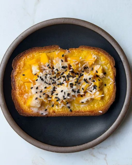 Mango sticky rice custard toast topped with coconut and sesame seeds