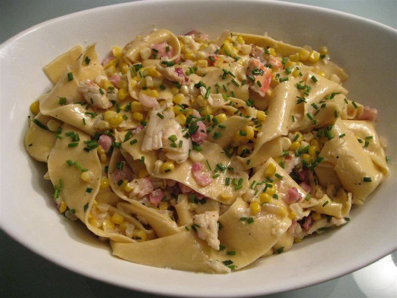 Pappardelle with corn, lobster, pancetta, and chives in a shallow white bowl