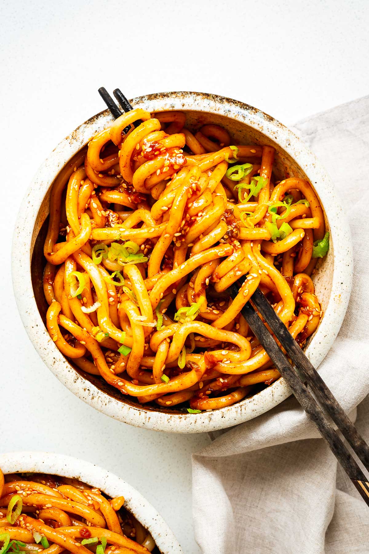 Bowl of spicy creamy udon noodles topped with green onions and sesame seeds